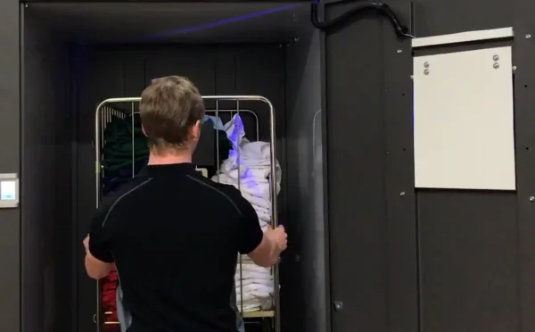 Industri arbetare med svart t-shirt scannar en hel tvättvagn med rfid märkta arbetskläder i en Q-Cabin från ACG Pulse på några sekunder.