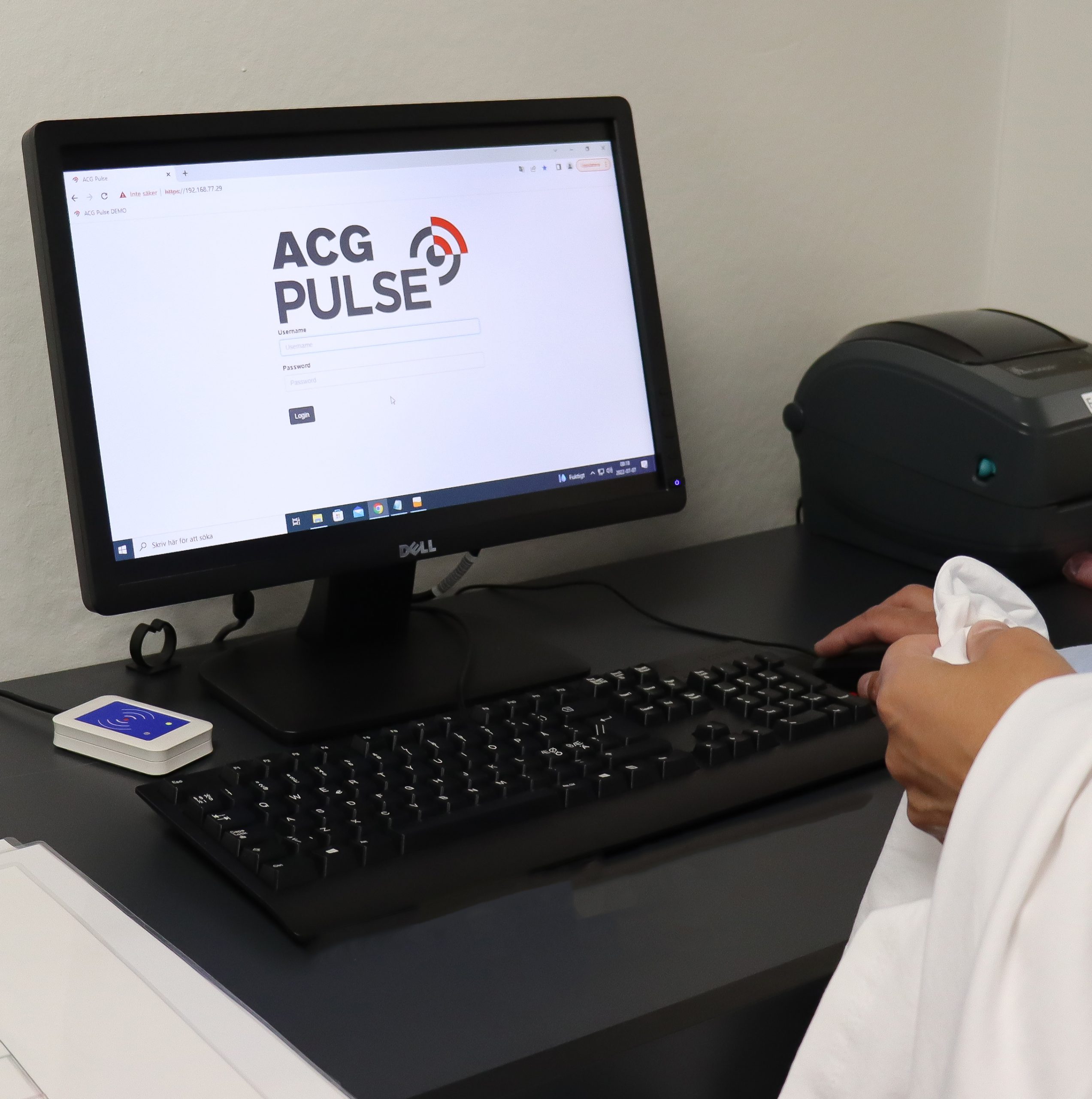 en hand som registrerar en vit t-shirt i en Praktisk registreringsstation för RFID en datorskärm visar information och tangentbord ligger på svart skrivbord